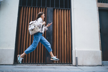Stylish lady using smartphone while rushing and running along pavement