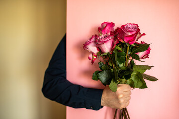 A man's hand in a blue shirt holds a bouquet of roses on a pink background.