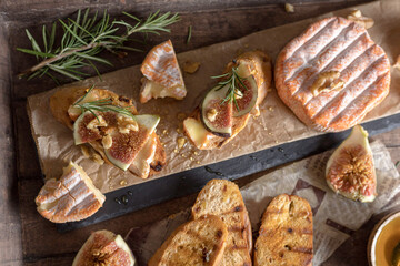 Crostini on a wood backghround with camembert ,figs ,honey  and rosemary .
Cheese delisious board 