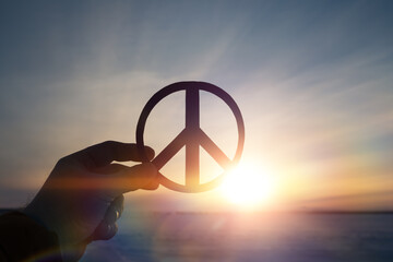 Peace sign symbol in the hand of a man on the background of the sunset. - obrazy, fototapety, plakaty