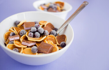 Pancake cereal in a plate with blueberries and chocolate on a purple table.Trendy modern breakfast with little pancakes.