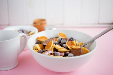 Pancake cereal in a plate with blueberries and chocolate on a pink table.Trendy modern breakfast with little pancakes.