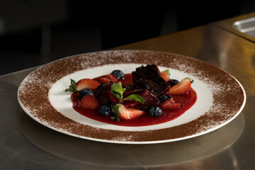 Close up shot of chocolate muffin with syrup and strawberry pieces on white plate decorated with cocoa powder