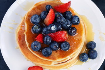 Pancakes with blueberries, strawberries, honey on a blue background
