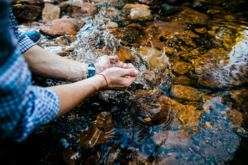 wash your hands in a mountain stream. the young man rolled up his sleeves with his hands in the water. Pure crystal water. wash in the creek. Outdoors. wet the watch on the hand.
