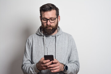 Portrait of young  man listening music on earphones with mobile phone  white wall