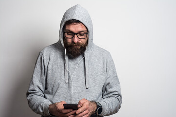 Portrait of young  man listening music on earphones with mobile phone  white wall