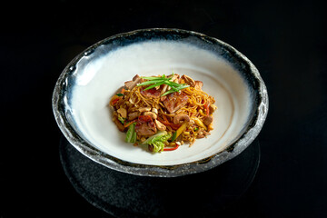 Sweet and sour noodles with pork, peanuts, vegetables and onions, served in a white bowl. Wok noodles. Isolated on a black background. Street thai food
