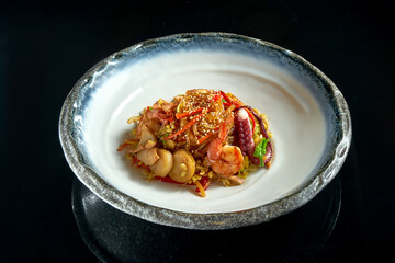 Glass rice noodles in sweet and sour sauce with shrimp, scallops, octopus and squid, served in a white bowl. Wok noodles. Isolated on a black background. Street thai food