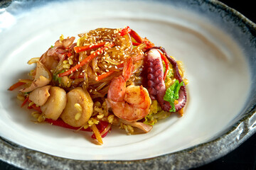 Glass rice noodles in sweet and sour sauce with shrimp, scallops, octopus and squid, served in a white bowl. Wok noodles. Isolated on a black background. Street thai food
