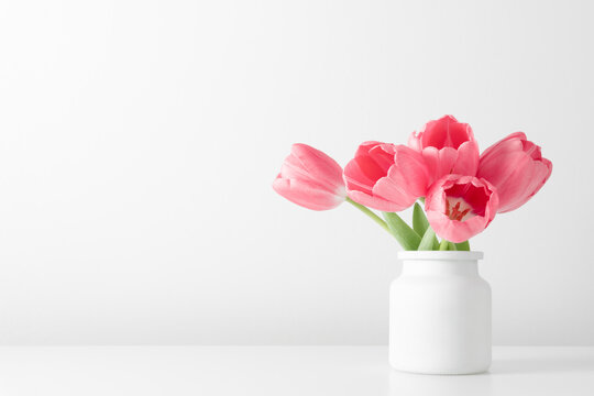 Pink tulips, spring flowers in vase on white table. Front view. Place for text, copy space, mockup