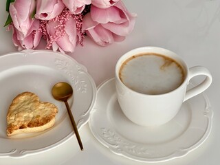 Morning breakfast with cup of coffee and biscuits in the background pink flower tulips