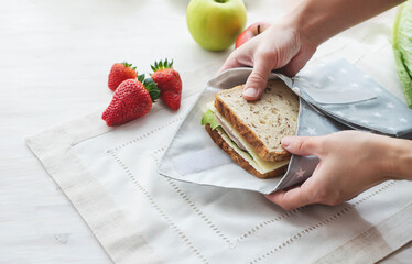 Person hands wrapping whole grain sandwich wrapped in reusable bag. Zero waste ecologic concept