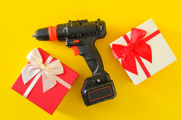 Handheld cordless power drill, hand battery screwdriver and gift boxes on yellow background. Concept of gift surprise for men, top view