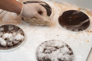 The process of washing the stove with a sponge and rubber gloves