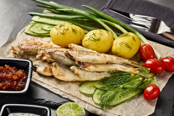 Fried smelts serving with potatoes, vegetables, lime and sauces. Grey slate background. Top view