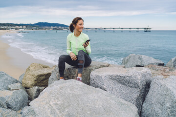 Happy young woman with smartphone resting on seashore