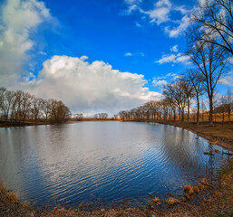 landscape with pond, and reflection in water beautiful sky, dry reeds and early spring trees