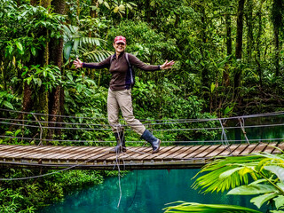 Tourist walks over a suspension bridge in Tenorio Volcano National Park, Costa Rica. - obrazy, fototapety, plakaty