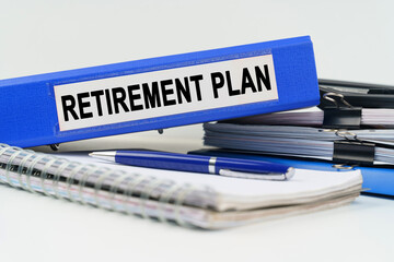 On the table are a notebook, a pen, documents and a folder with the inscription - RETIREMENT PLAN