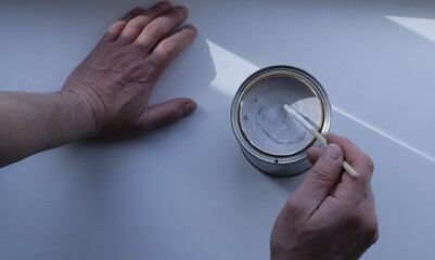 male hands stirring dark color in thick white paint in a tin can using a thin wooden stick top view, diluting a gray shade of paint to paint the surface in the process of interior renovation
