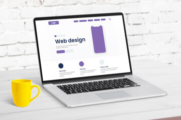 Web design studio page concept with website elements on laptop computer. Clean desk with yellow coffee mug beside