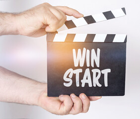 Obraz premium On a white background, a man holds a clapperboard in his hands on which it is written - WIN START