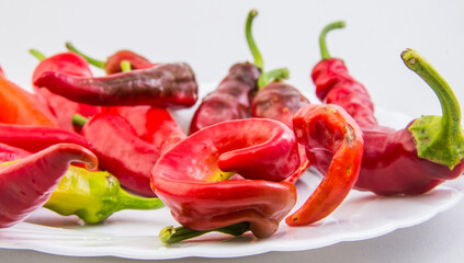 Pods of fresh hot red pepper on a white plate on a white background.