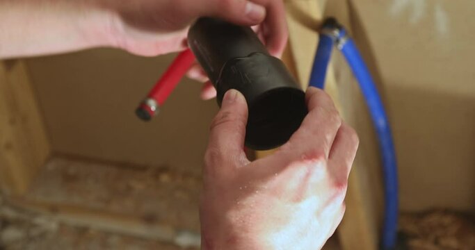 Plumber jointing glue PVC sewage drain pipes on a house under construction
