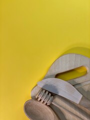 On a yellow background is a cutting board and wooden cutlery
