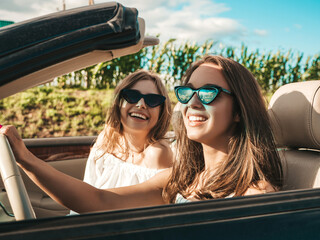 Portrait of two young beautiful and smiling hipster female in convertible car. Sexy carefree women...