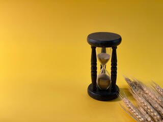 On a yellow background there is an hourglass measuring the time, there is a barley grain