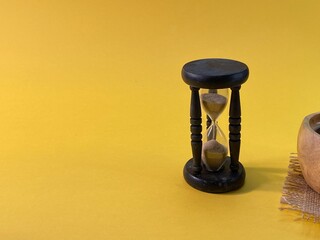 On a yellow background stands an hourglass measuring the time, next to a jute napkin stands a wooden cup with coffee