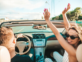 Portrait of young beautiful smiling hipster female and her boyfriend in convertible car. Sexy...