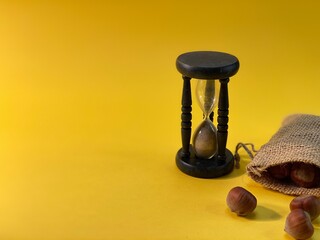 On a yellow background there is an hourglass measuring time, next to it is a jute sack with hazelnuts sprinkled on it