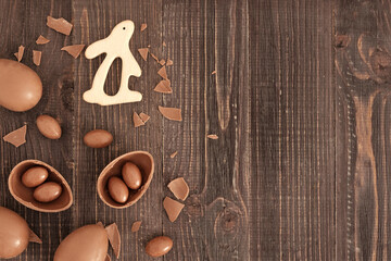 Flat lay of chocolate eggs, pieces of chocolate and candies and bunny on the wooden background. Handmade easter decoration. Copy space, place for text. Eater gift.