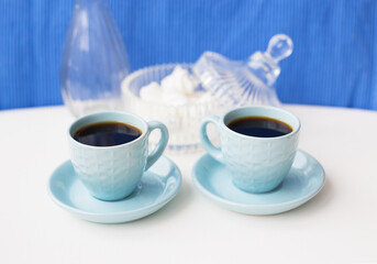 Two blue coffee cup on the table with a vase and saucer with marshmallows