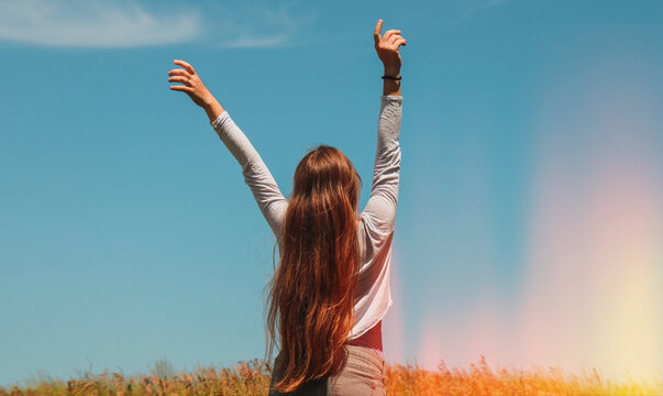 A long-haired blonde in the middle of a field with wheat raised her hands up and enjoys the air and freedom.
