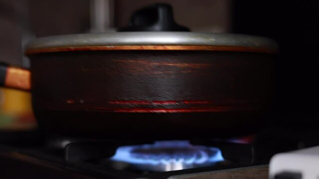 Male Hand Lighting The Fire At The Gas Stove And Putting A Frying Pan On The Blue Flame In Dark Background.