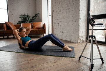 Young fit woman blogger in sportswear shoots video on phone as she does exercises at home in the living room.