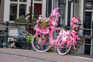 Fototapeta na wymiar Old vintage bicycle decorated with pink flowers on small bridge in old part of Amsterdam