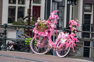 Fototapeta na wymiar Old vintage bicycle decorated with pink flowers on small bridge in old part of Amsterdam