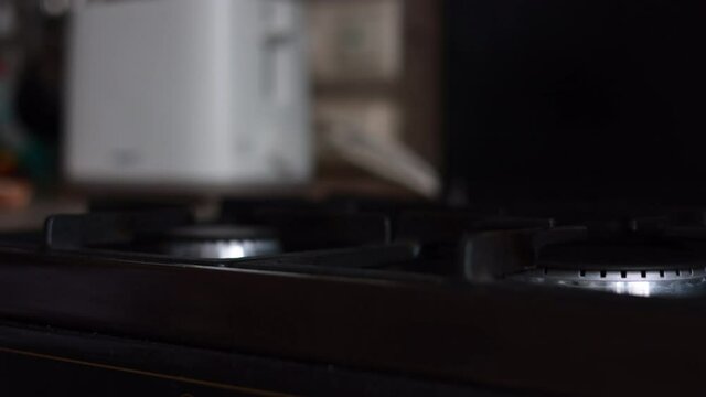 Male Hand Lighting The Fire At The Gas Stove And Putting A Frying Pan On The Blue Flame In Dark Background. Panning Dolly Slider Shot.
