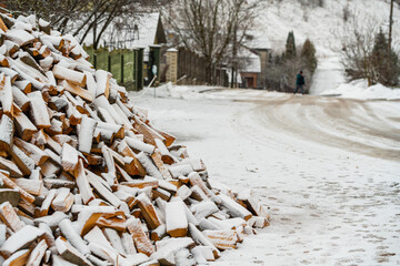 A pile of stuck firewood on the background of a snow-covered village street
