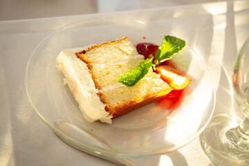 Slice of yellow sponge cake with thick white frosting, strawberry and sauce and garnished with a mint sprig
