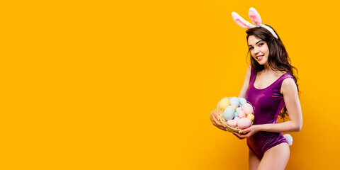 Attractive hot young woman wearing bodysuit and bunny ears holding basket with colored Easter eggs...