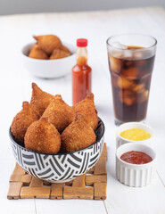 Typical brazilian snack coxinha on a plate with soda glass, ketchup, pepper and mustard