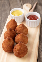 Typical brazilian snack coxinha on a wooden board with ketchup and mustard