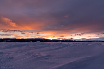 Fototapeta na wymiar Winter frozen lake scene in northern Canada on a stunning cloudy sunset afternoon in March with white snow, mountains in background and iconic Canadian landscape in the north. 