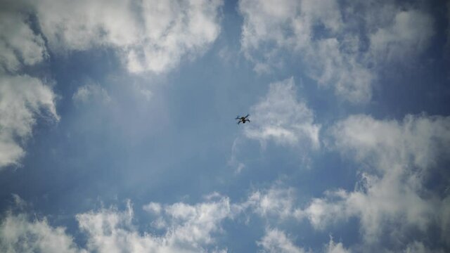 The drone flies against a background of blue sky and clouds, a view from below. The quadcopter with the camera hovers at a low altitude. Fast-rotating drone propellers.